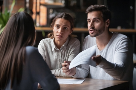 A couple discussing a document with a concerned expression while speaking to a professional across the table. | Curtis | Walton Law